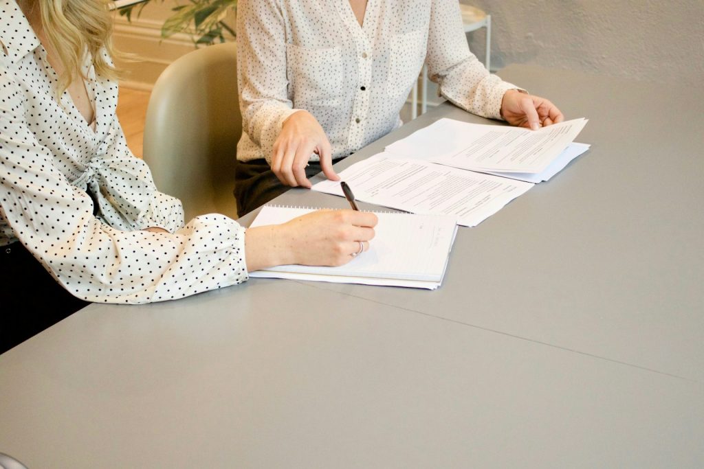 A woman signing papers while another woman looks on