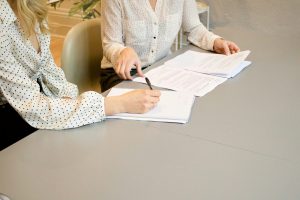 A woman signing papers while another woman looks on