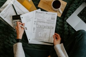A person reviewing tax documents with a calculator and laptop